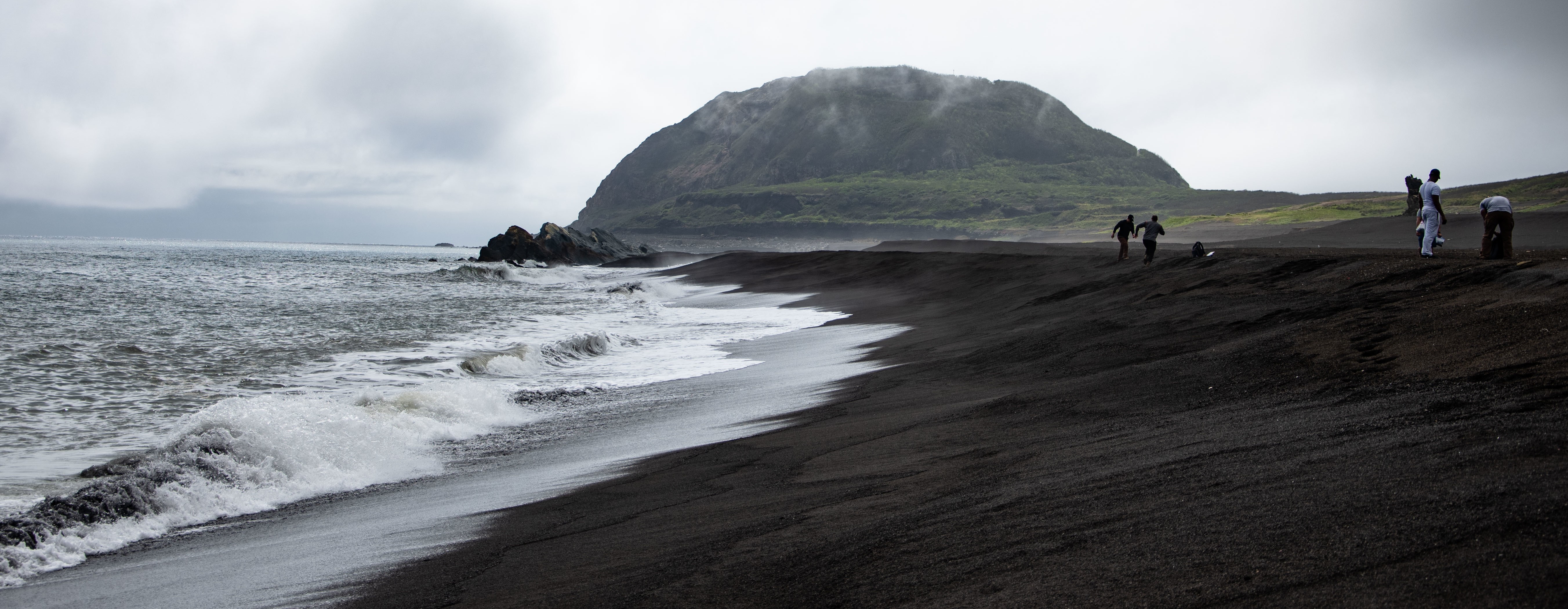 Waves on the black sands of Iwo Jima with an island in the distance.
