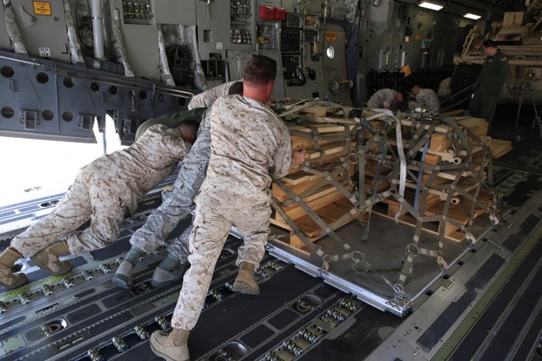 Five Marines working together to push a stack of pallets up an aircraft.