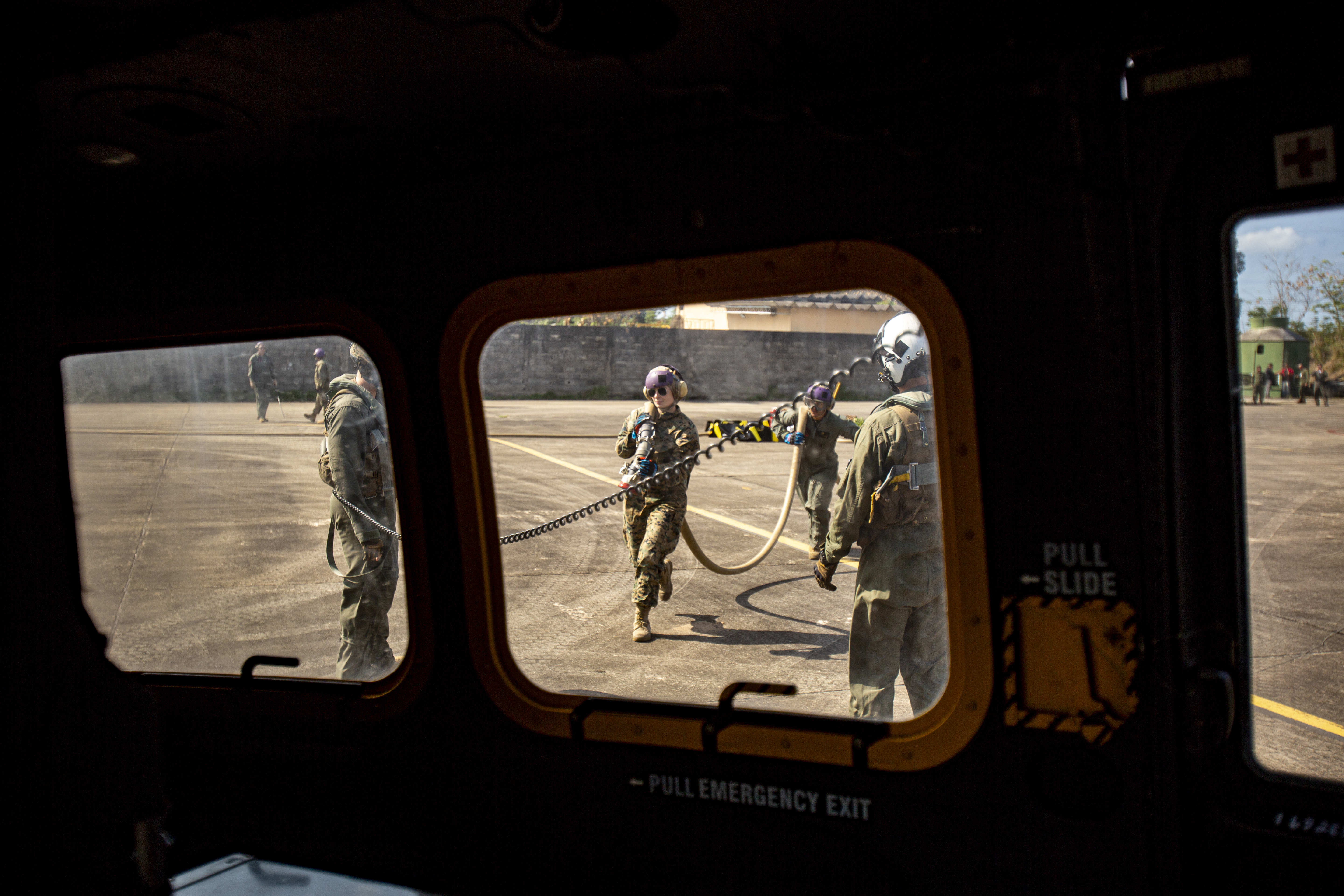 Looking out of small windows, three Marines on the ground working on an airplane.